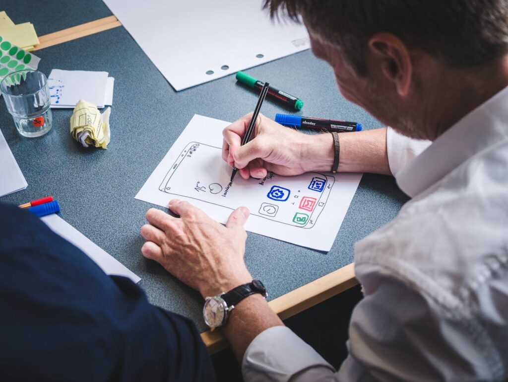 pexels-photo-3471423 A designer sketches a mobile app prototype on paper at an office desk, focusing on creativity and design.